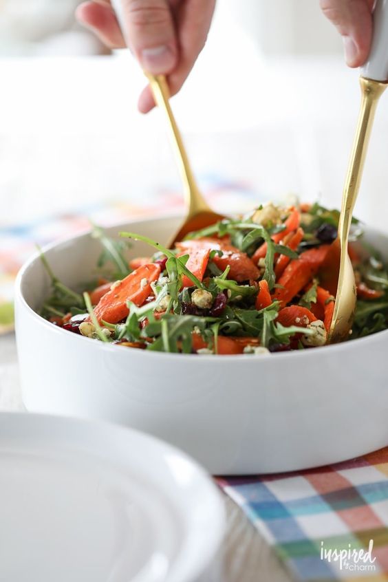 White bowl filled with carrot salad and two hands holding utensils to mix it