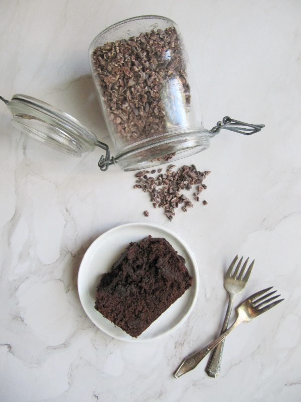cocoa nibs a jar laying on its side with a piece of chocolate bread on white plate and two forks