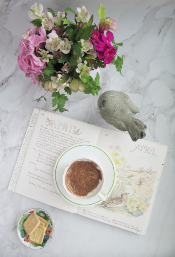 flatlay book open to April flowers concrete bird chocolate and cookies