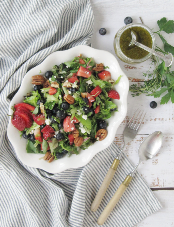 Strawberry and Fresh Herb Salad with Blueberries and Feta on a white plate sitting on a blue and white stripped towel with silverware-2