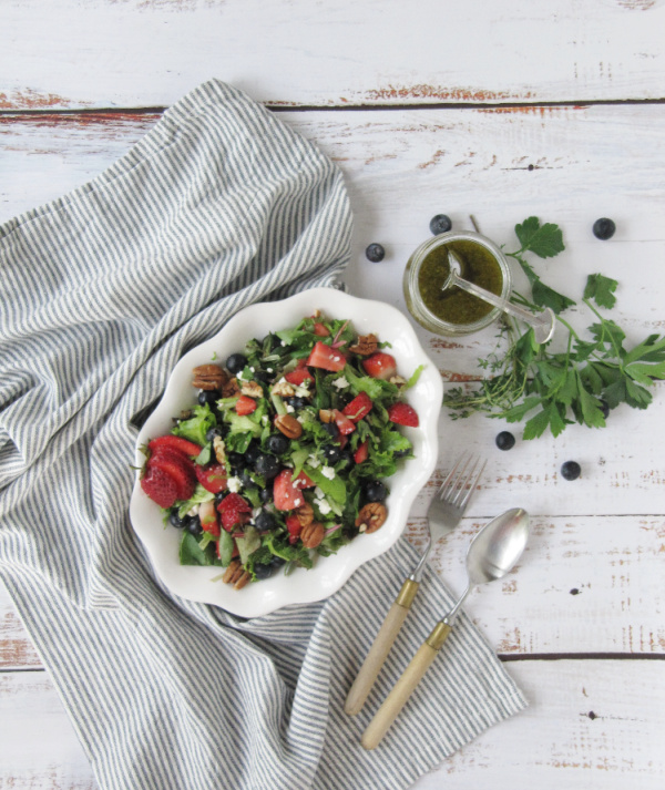 Strawberry and Fresh Herb Salad with Blueberries and Feta on a white plate sitting on a blue and white stripped towel.