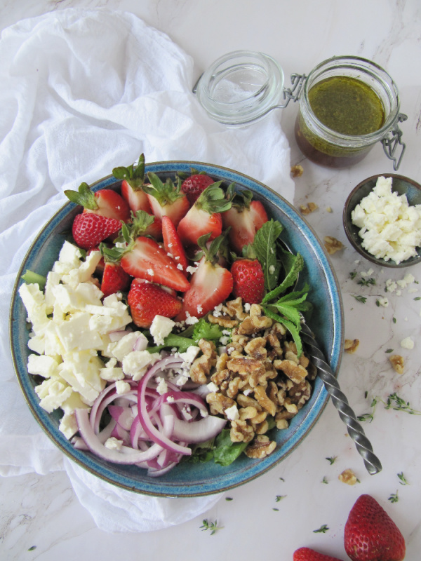 salad with red onions feta cheese strawberries and walnuts in a blue bowl