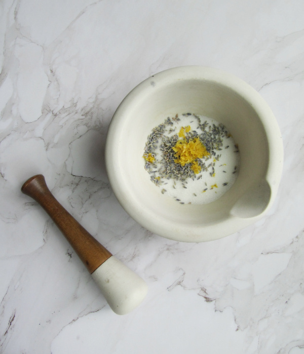 lemon lavender shortbread cookies lemon zest, lavender buds and sugar in a white marble mortal with a petal sitting on the side