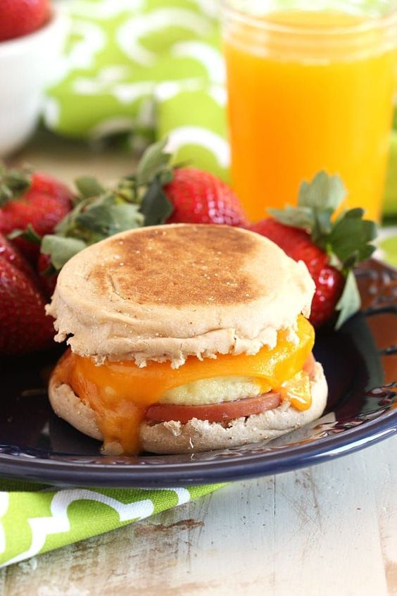 egg McMuffin sandwich on a blue plate with strawberries and a glass of orange juice
