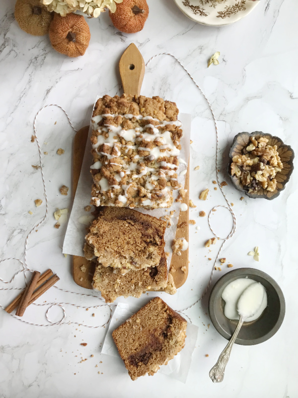 cinnamon swirl pumpkin bread with crumble topping on a wood cutting board sliced with cinnamon sticks and string pumpkins