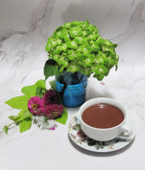 green hydrangea in a blue glass with sweet potato vine pink zinnias and cup of hot chocolate