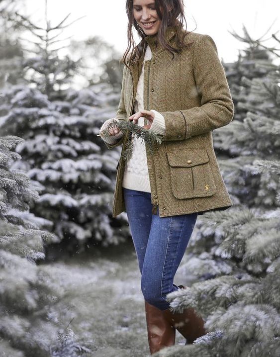 woman in a tweed jacket and jeans standing among snowy trees