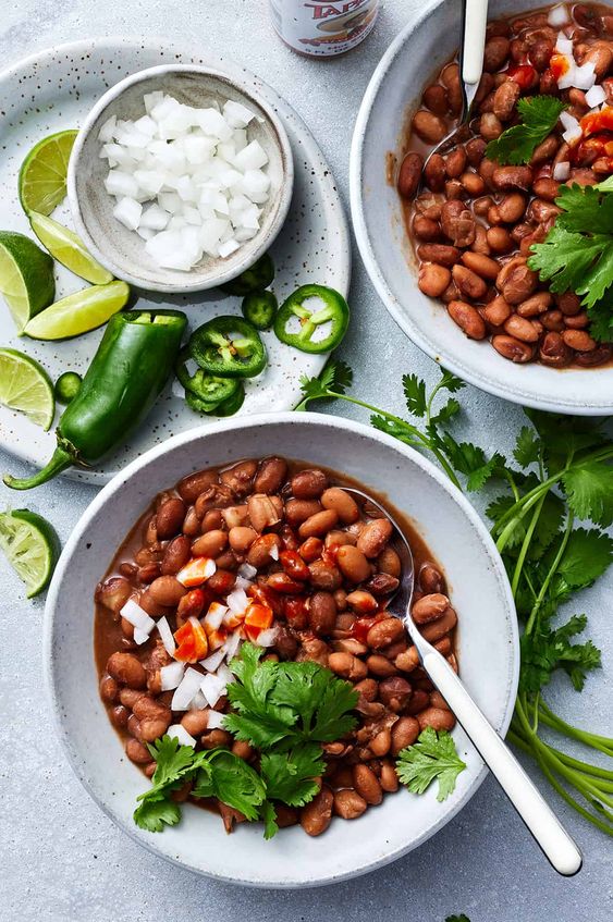 Friday Favorites Two white bowls filled with pinto beans and a plate that has lime slices and jalapeño as well as white onions.