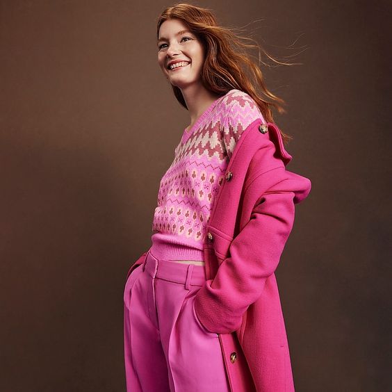 friday favorites smiling woman wearing a pink an white cable knot sweater with a pink coat and pants.