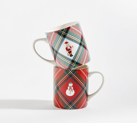 1 green and white plaid cup on top of a red and green plaid cup one has a nutcrackerr one has a snowman.
