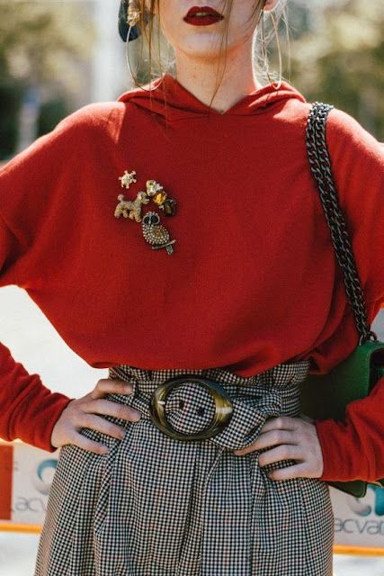 woman in a red sweater check trousers wearing 5 brooches