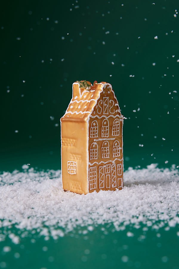gingerbread house ornament sitting in fake snow with a green background. 