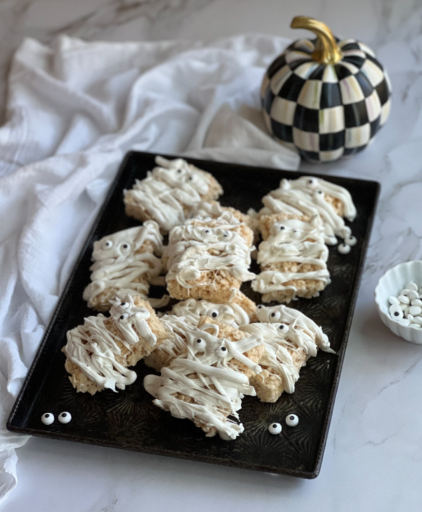 Mummy Rice Krispie treats on a baking pan with a black and white pumpkin. 