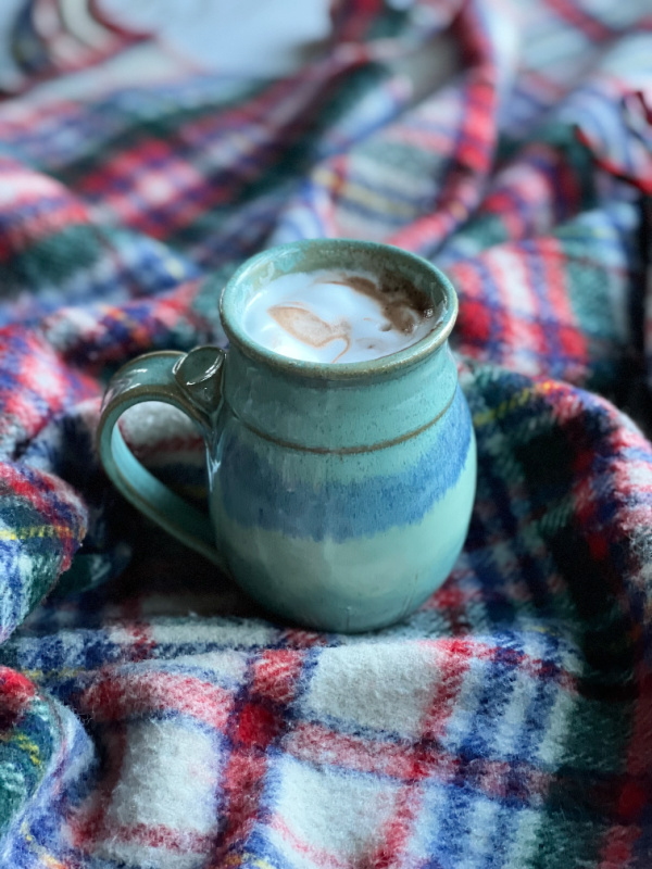 pottery mug filled with hot chocolate on a vintage plaid blanket