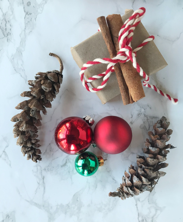 two pinecones the red ornaments a green ornament and two brown paper packaged ties with red and white twine