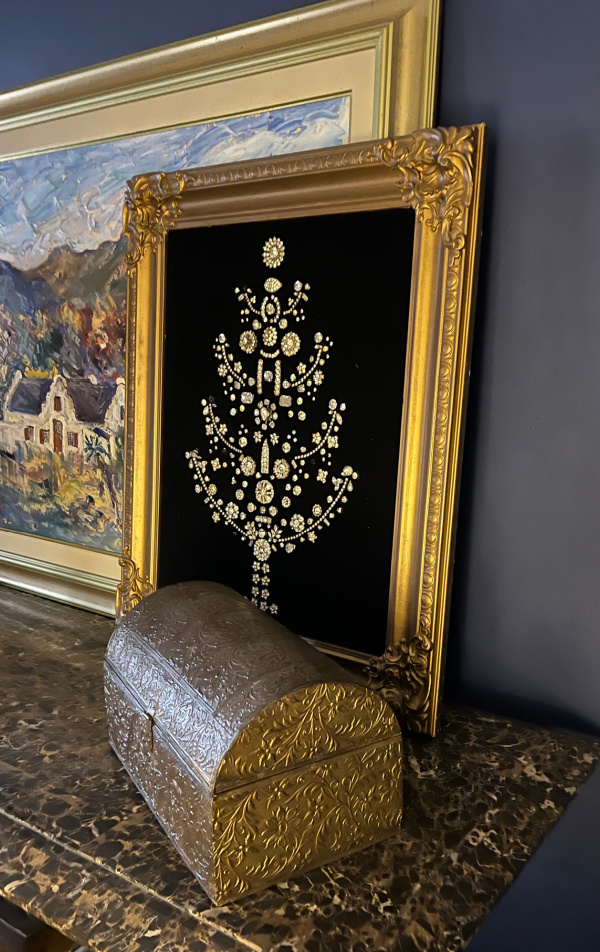 Christmas tree made from rhinestone jewelry on black velvet leaning on a landscape painting.