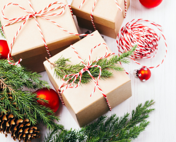 christmas gifts wrapped in brown paper with red and white twine with evergreens and red balls.