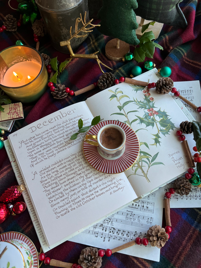flatlay December with book music cup of chocolate holiday ornaments holly