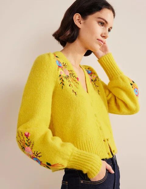 A woman wearing a bright yellow sweater with colorful embroidery.