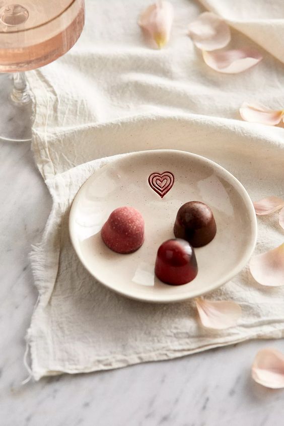 A mug with a heart filled with hot chocolate and a plate with a heart with 3 pieces of chocolate. 