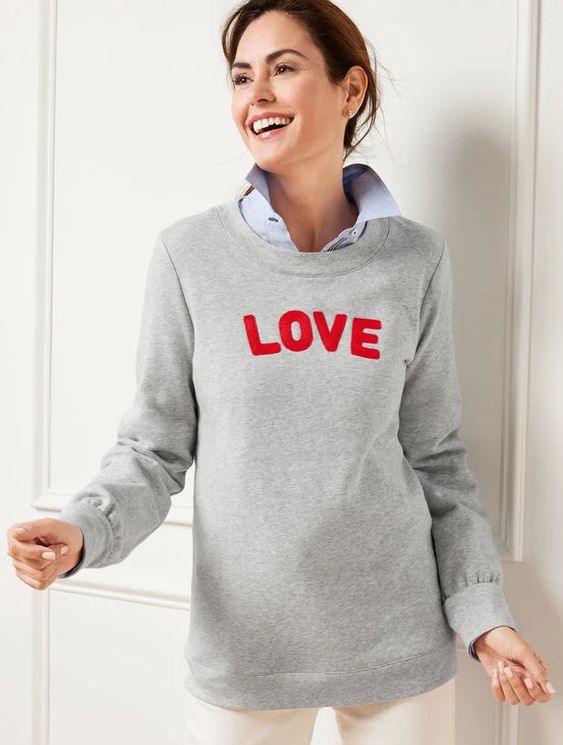 Woman wearing a gray sweatshirt with LOVE spelled in red letters. 