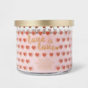 A pink candle in a clear glass container with pink and red hearts.