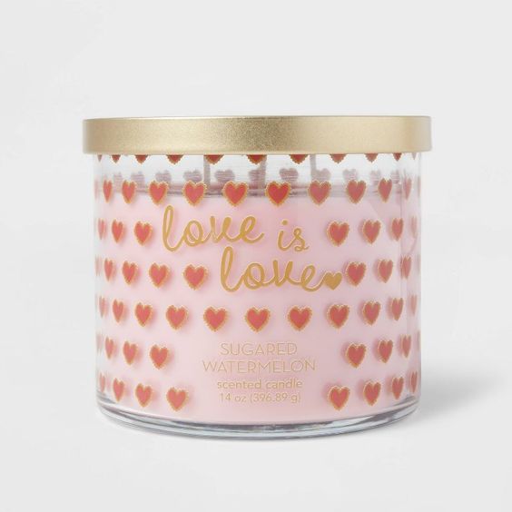 A pink candle in a clear glass container with pink and red hearts. 