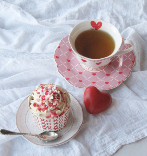 Cup of tea in heart cup and a cupcake with a red heart laying on the side.