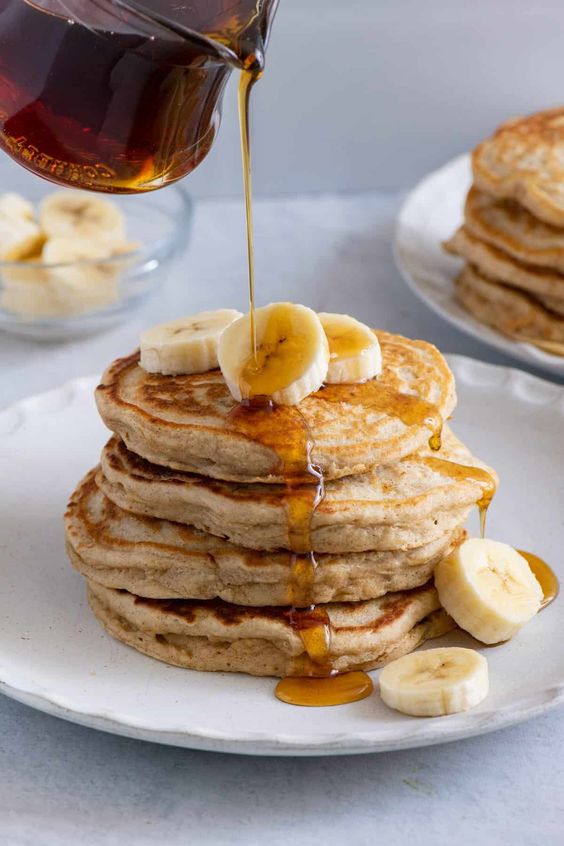 Fluffy Banana Pancakes on two plates stacked high withy banana slices and syrup.