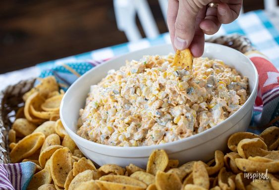 A white bowl filled with corn dip surrounded by Fritos. 
