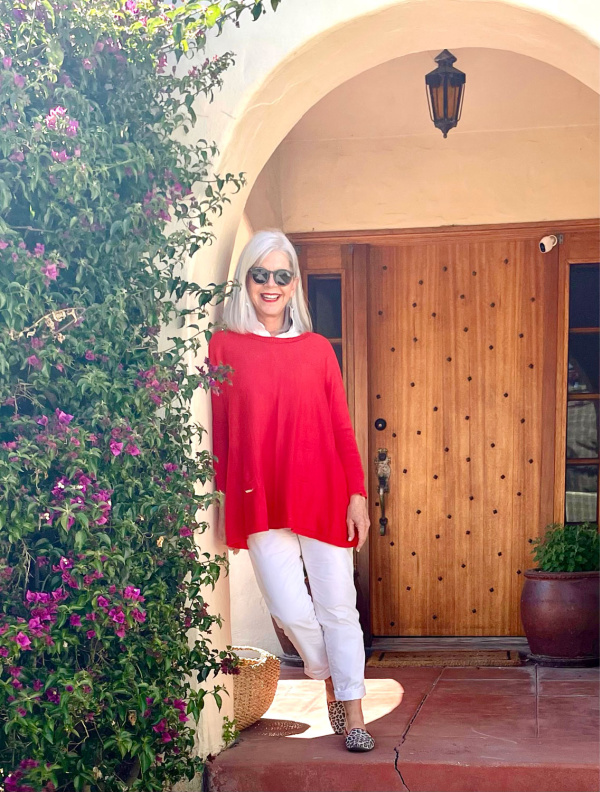 Woman wearing a red wrap and white jeans leaning against a wall.