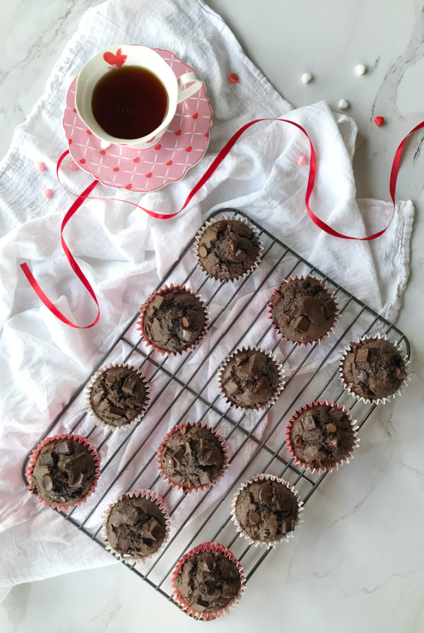 Double chocolate muffins, 12 on a wire rack with a cup of tea on a saucer in the top left corner.