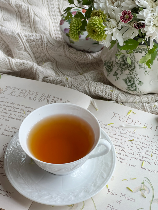 Photos with cup of tea book and flowers in a green transfer ware pot.
