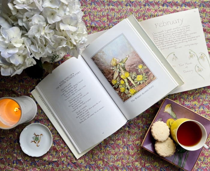 February flatlay with fairy books, tea, flowers and a candle.