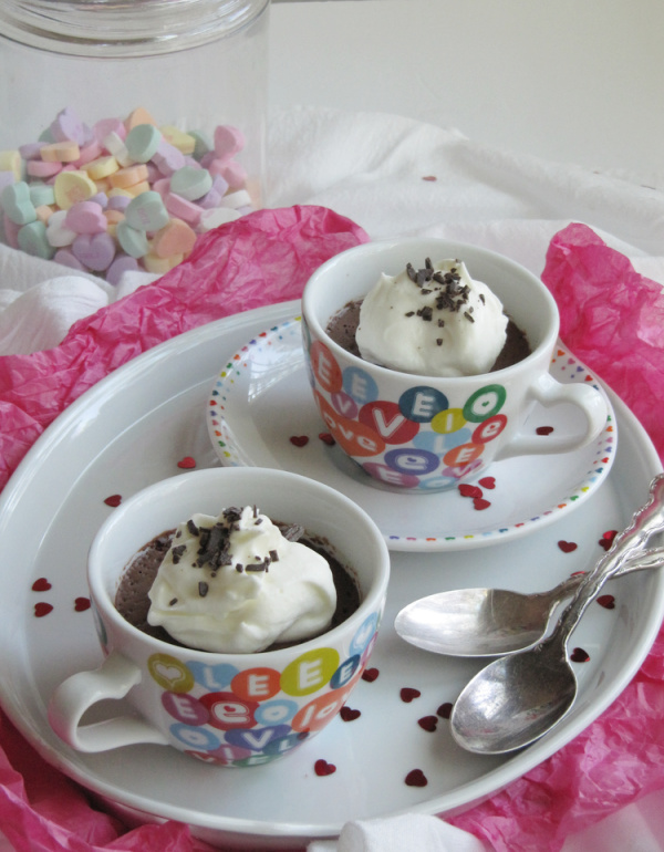 White cups with colored hearts sitting on a shite porcelain tray with 2 silver spoons. 