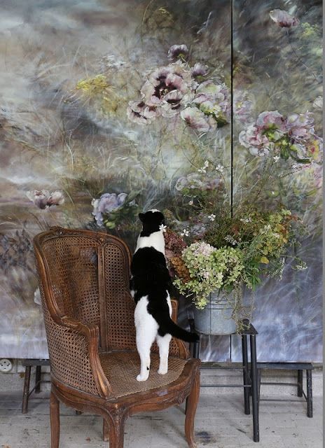 cat sitting on a caned chair in front of a mural of flowers.