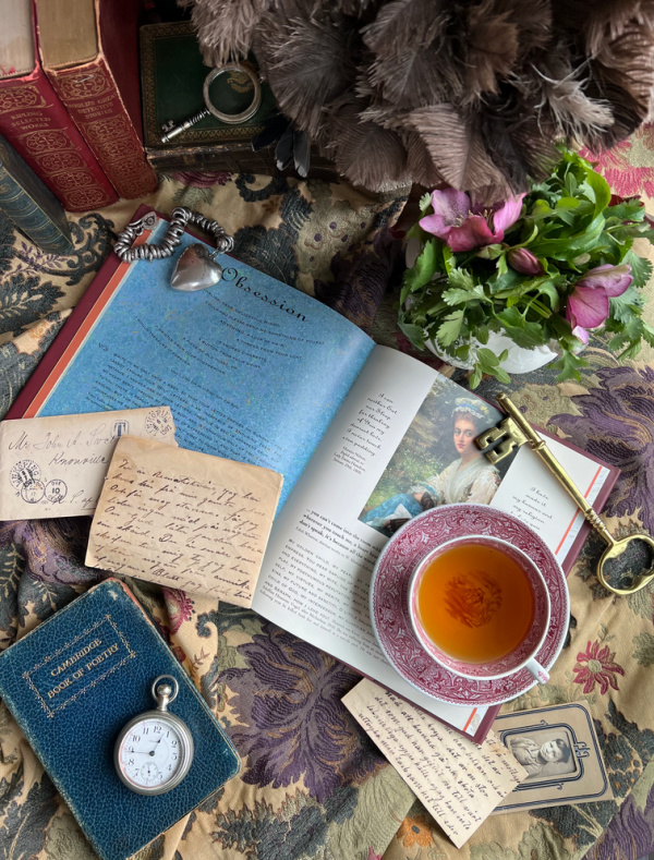 flatlay with poetry books, cup of tea, vintage letters, a heart, brass key, flowers on brocade .