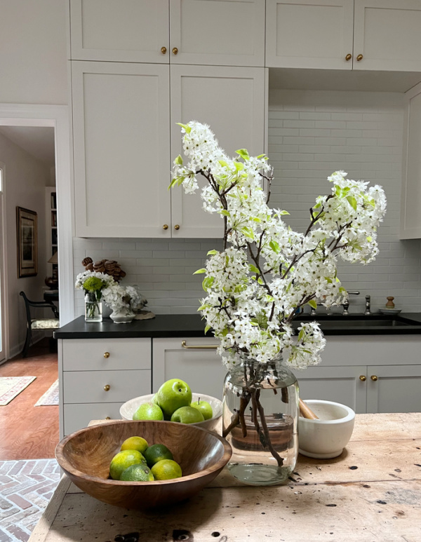 pear blossoms in a glass jar in the kitchen by a bowl of green apples and limes.