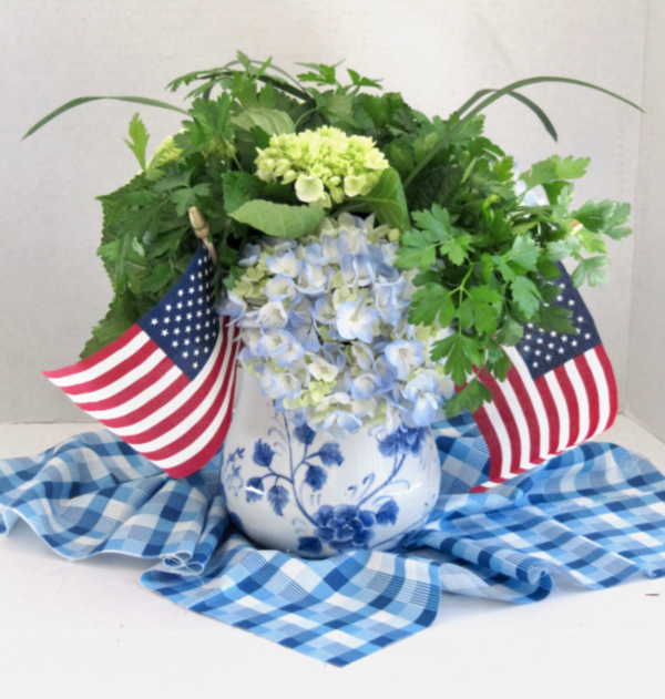 blue hydrangeas in a blue and white vase with 2 American flags.