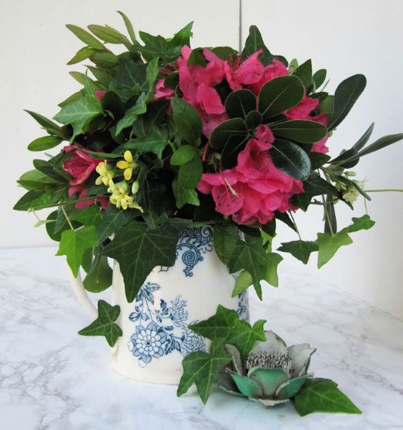 Mothers day flowers, pink with green and yellow leaves in a blue and white transfer ware pitcher with a green flower frog on the side. 