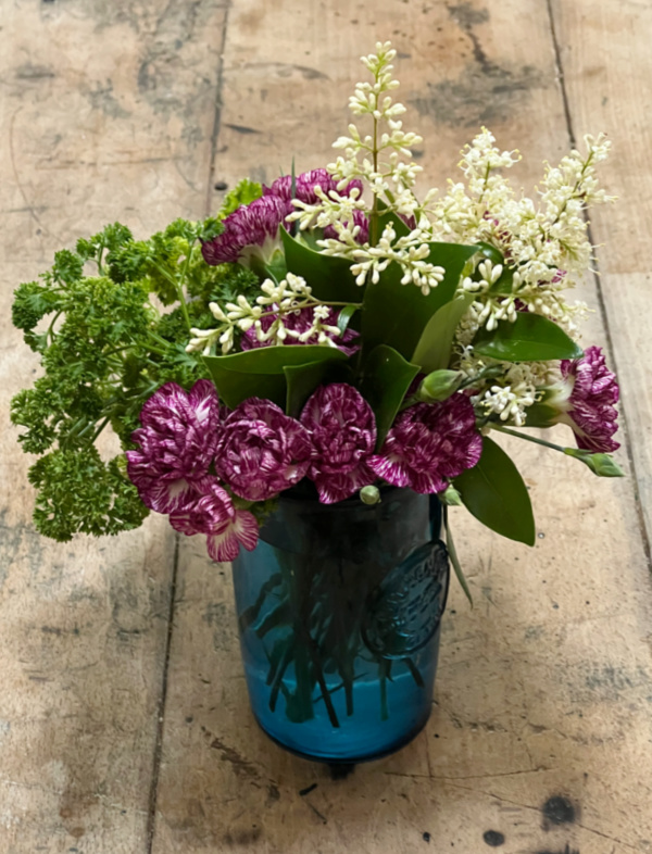 purple carnations white lilacs and green parsley in a blue glass.