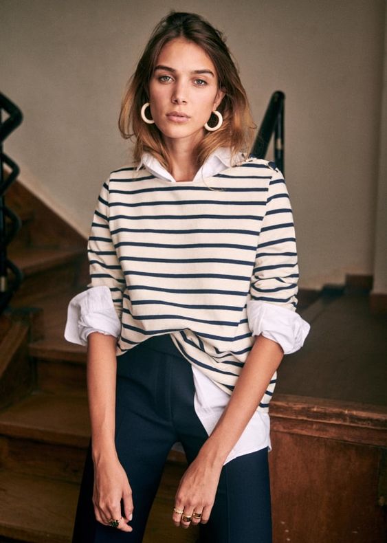 Woman wearing a white blouse with a blue and white sweater and blue pants.