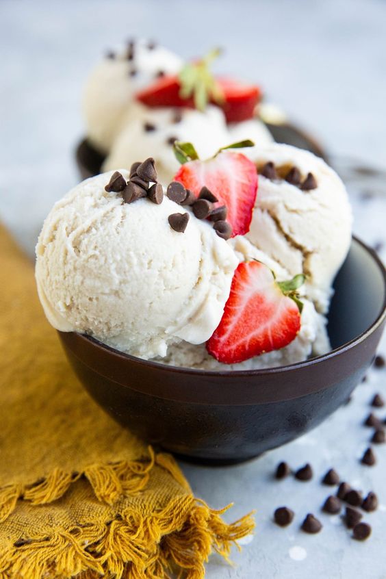DAIRY-FREE VANILLA ICE CREAM in a brown bowl with strawberries and chocolate chips.