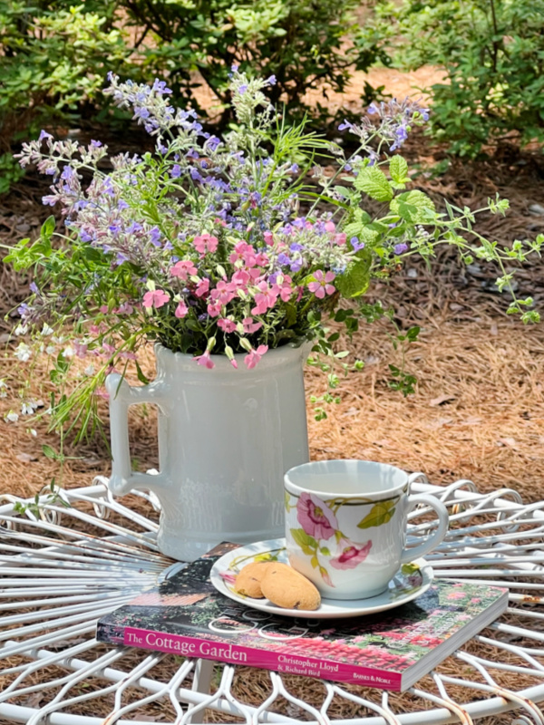 wildflowers in a white pitcher with a cup of tea and a cottage garden book