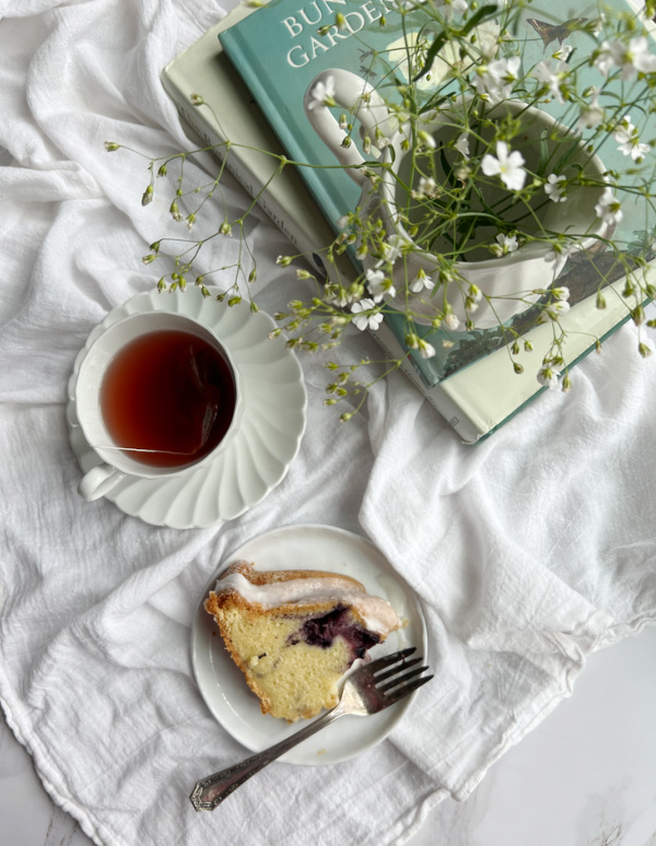 Blueberry Swirl Bundt Cake on a plate with a cup of tea and a pile of books with white flowers.