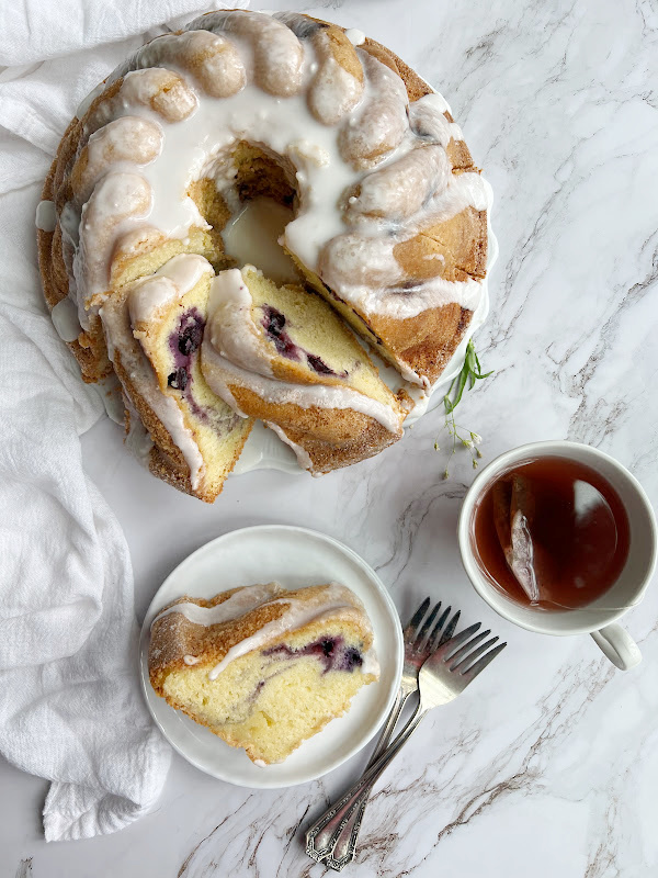 Blueberry swirl Bundt Cake on a plate cut into pieces with a pice on a separate white plate next to a cup of tea.