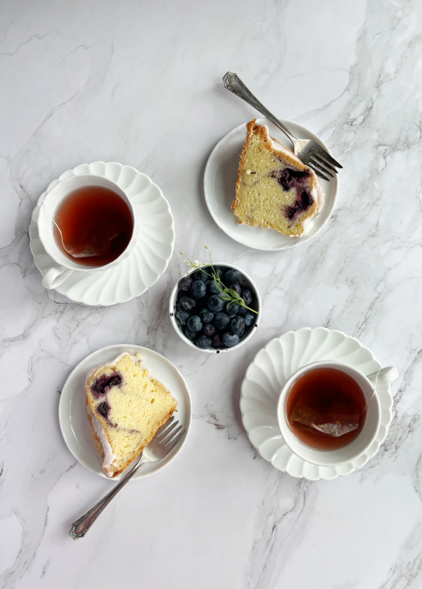 blueberry swirl bundt cake on 2 plates with 2 cups of tea and a bowl of blueberries