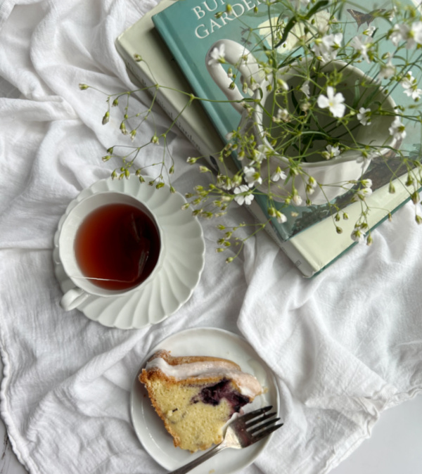 cup of tea with a piece of coffee cake and a pile of books.