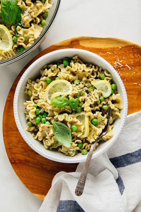 A white bowl with peas, pasta and pesto sauce. 