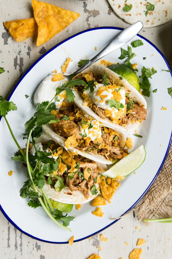 Slow Cooker Chili Lime Chicken in tacos on a white oval tray. 